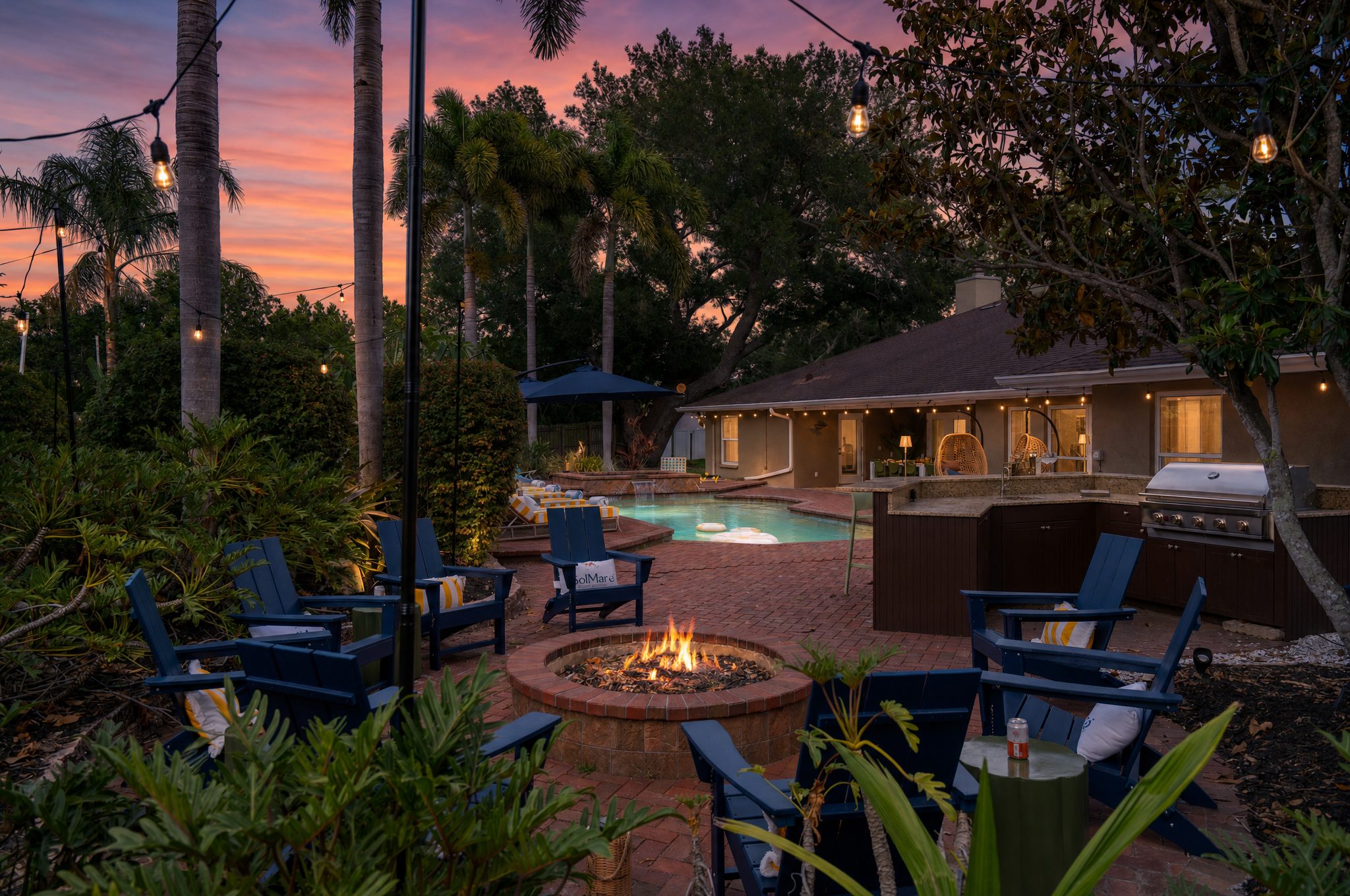 Vacation rental outdoor living space with fire pit, Adirondack chairs, outdoor kitchen, and pool at twilight — Orlando Home Photography
