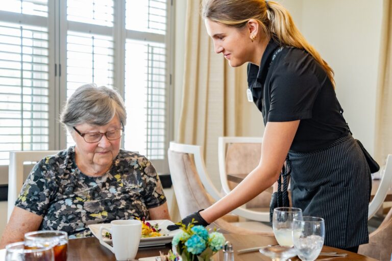 Server bringing lunch to a resident in a senior living dining room