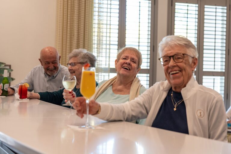 Residents laughing and sharing drinks at a senior living community bar