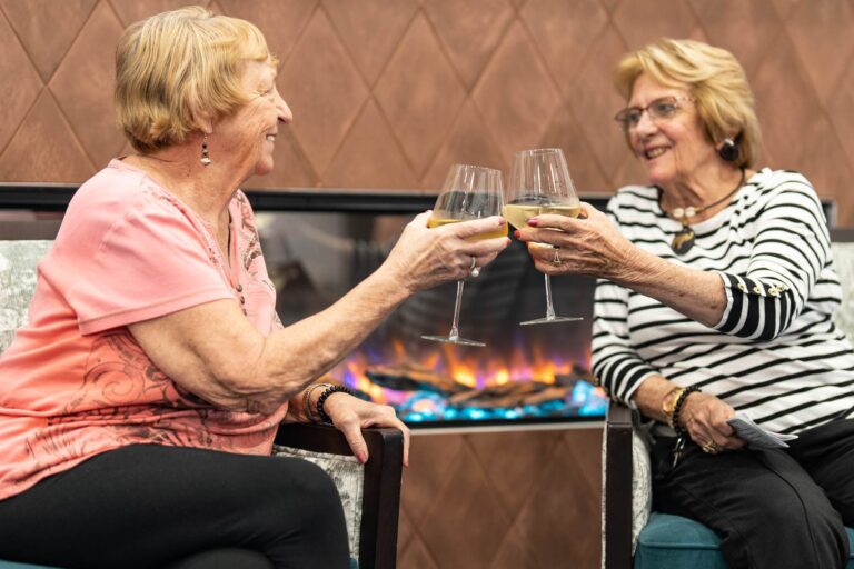 Two senior living residents sharing a toast by the fireplace